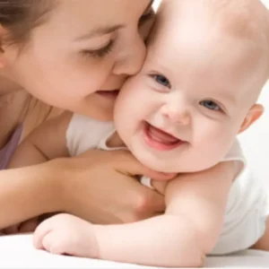 Mother kissing smiling baby on bed.