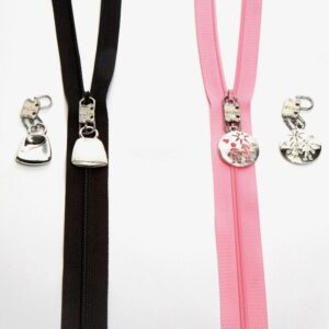 Two zippers with decorative handbag-shaped pulls on black and pink fabric.