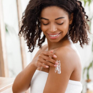 A woman applying lotion to her shoulder with a smile.
